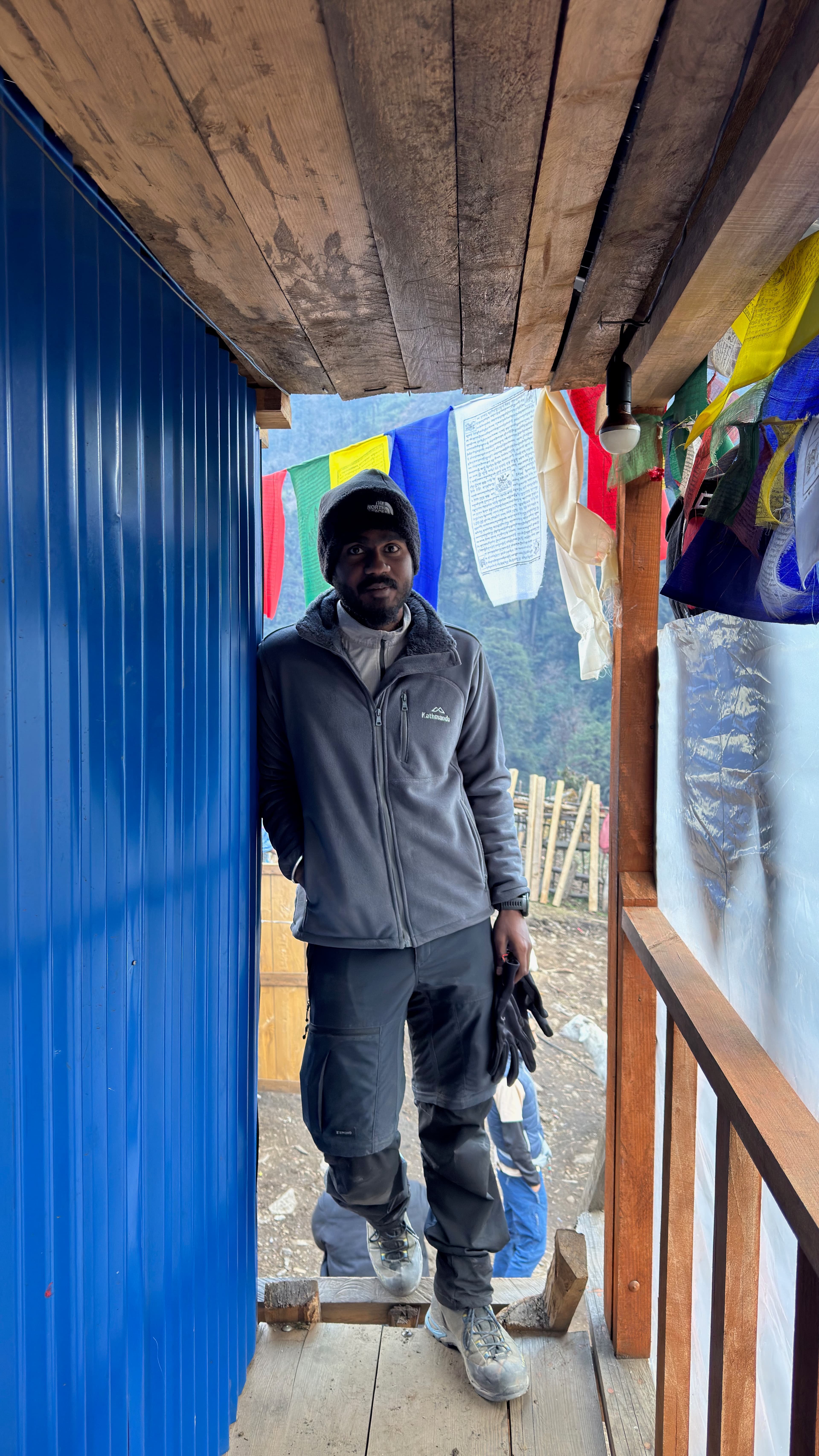 Vivek standing beside prayer flags in a mountain shelter